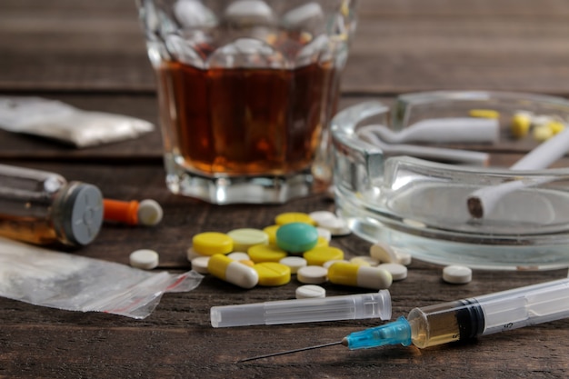 Foto várias drogas viciantes, incluindo álcool, cigarros e drogas em uma mesa de madeira marrom. conceito de toxicodependência