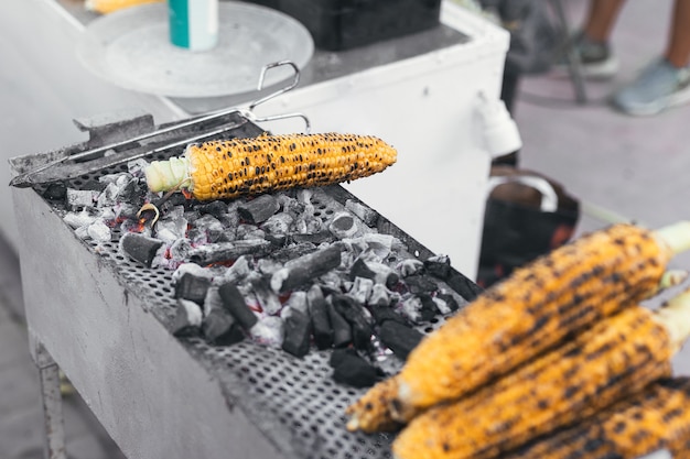 Várias espigas de milho assando no carvão em uma barraca de comida de rua