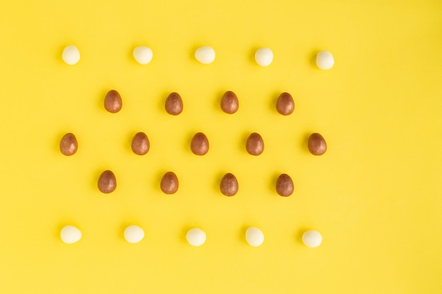 Varias filas de huevos pequeños hechos de chocolate blanco y negro sobre fondo amarillo Símbolo de la tarjeta de felicitación de Pascua de celebración Domingo de Cristo Espacio de copia de composición de vacaciones para felicitaciones de texto