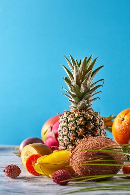 Varias frutas exóticas hojas de palmera sobre una mesa de madera gris