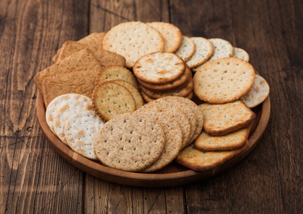 Varias galletas crujientes orgánicas de pan plano plano de trigo, centeno y maíz con sésamo y sal en placa redonda sobre fondo de madera.