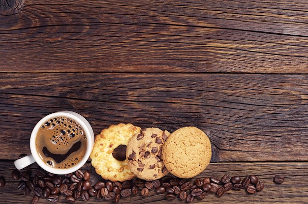 Varias galletas dulces y una taza de café caliente en la mesa de madera oscura, vista superior