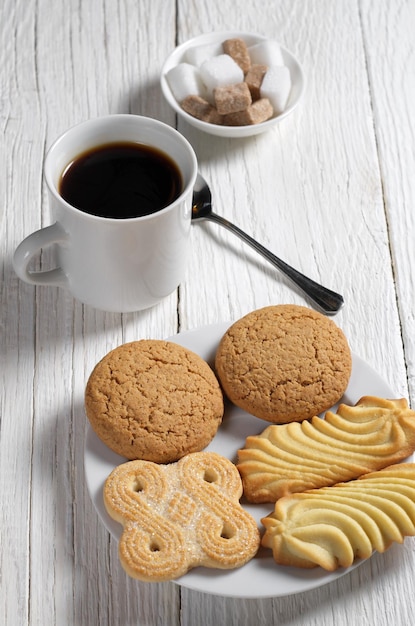 Varias galletas en plato y taza de café para el desayuno en la mesa de madera blanca