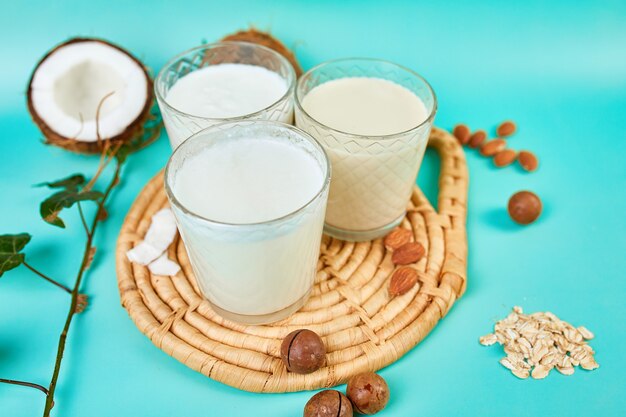 Varias leches e ingredientes veganos a base de plantas, leche no láctea, tipos alternativos de leches veganas en vasos sobre una superficie azul con espacio de copia