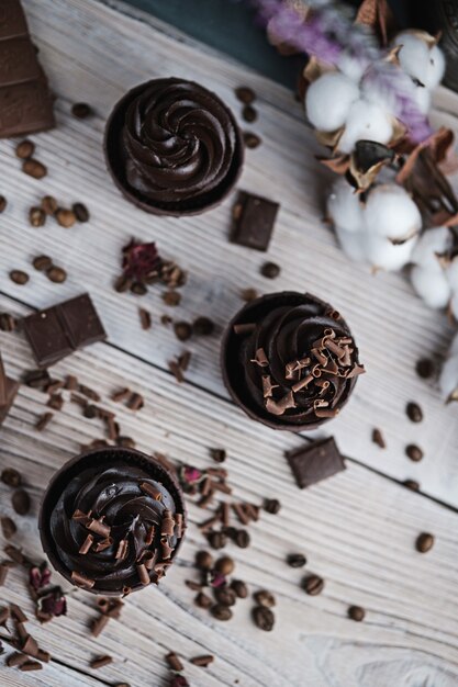 Varias magdalenas o cupcakes con crema en forma de chocolate en la mesa blanca. Vela festiva arde en un pastel de chocolate. Hay chispas de chocolate esparcidas cerca