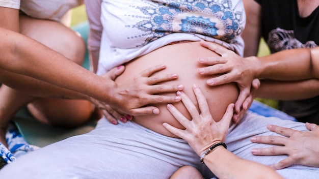 Várias mãos tocam a barriga de uma mulher grávida