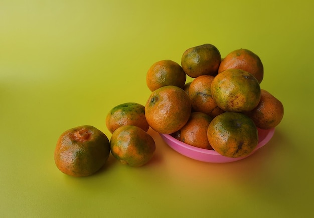 Varias naranjas en un plato rosa sobre un fondo amarillo 01