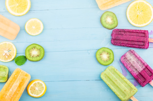 Varias paletas de frutas se colocan en el fondo de la tabla de madera azul, paletas de kiwi, paletas de naranja, paletas de fruta del dragón, paletas de melón