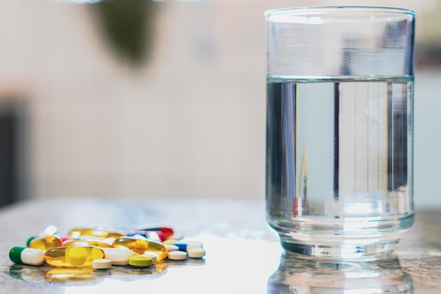 Varias pastillas en la mesa junto al vaso de agua