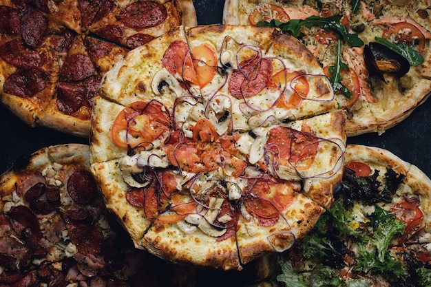 Várias pizzas com carne e legumes em um fundo escuro