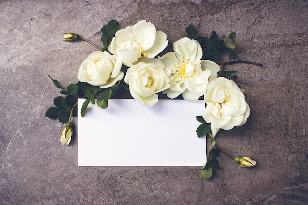 Varias rosas sobre fondo blanco de madera rústica con tarjeta vacía para mensaje de saludo.