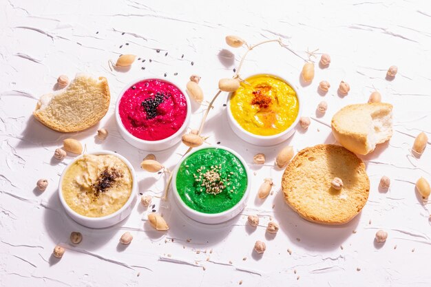 Varias salsas de hummus, la disposición plana de hummus en diferentes colores con espinacas, remolacha, cúrcuma y verduras, snack vegano. Fondo de masilla blanca, vista superior