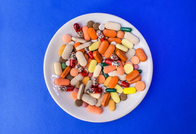 Varias tabletas de medicina, cápsulas y píldoras en platillos con fondo azul.