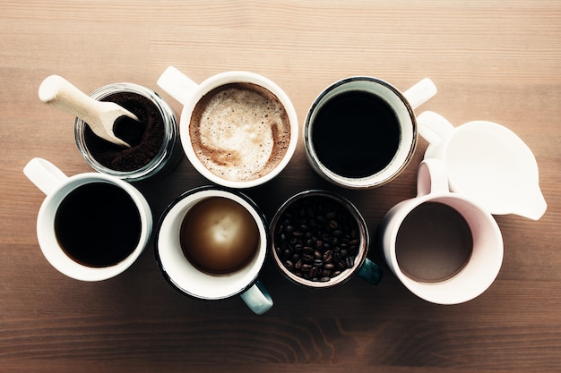 Varias tazas de café, leche, frijoles y café molido en tarro sobre fondo de madera. Foto de alta calidad