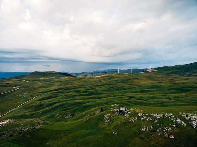 Várias turbinas eólicas em colinas verdes nas montanhas de montenegro contra o céu nublado e chuvoso