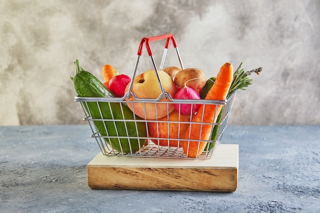 Varias verduras y frutas en una canasta de supermercado en un podio de madera