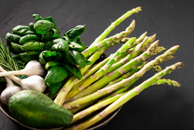 Varias verduras verdes sobre un fondo oscuro Espárragos espinacas aguacate ajo Concepto de comida vegetariana