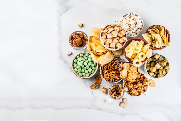 Foto variation verschiedene ungesunde snacks cracker, süß gesalzenes popcorn, tortillas, nüsse, strohhalme, bretsels