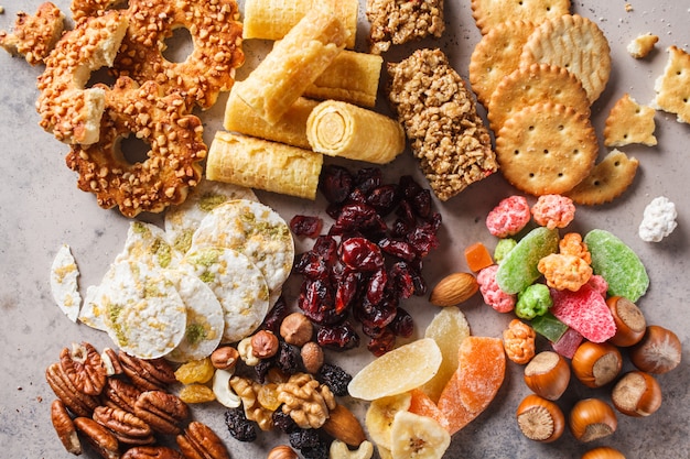 Variedad de aperitivos y dulces sobre fondo gris. Waffles, nueces, dulces, galletas, papas fritas y frutas, vista desde arriba.