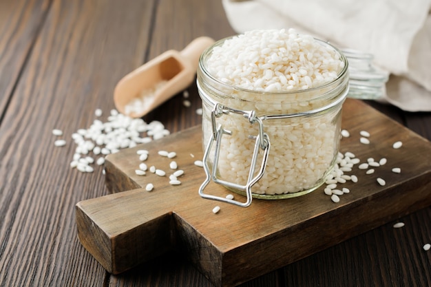 Variedad de arroz blanco crudo Arborio para platos de risotto italiano en frasco de vidrio sobre superficie de madera oscura.