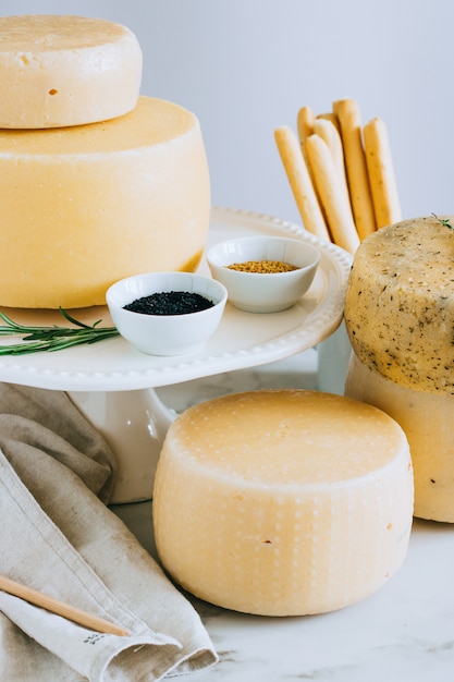 Una variedad de cabezas de queso Cachotta con comino negro, fenogreco y hierbas en un soporte para pasteles