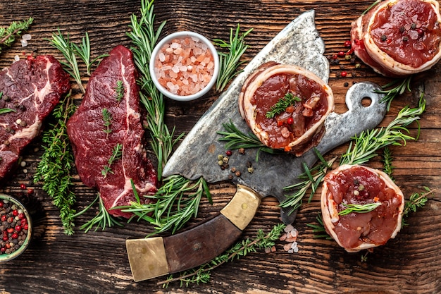 Variedad de filetes de carne de res cruda para asar a la parrilla con condimentos y hierbas en carnicero de carne vieja sobre fondo de madera oscura. banner, vista superior de la receta del menú.