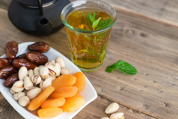 Variedad de frutos secos con un vaso de té de menta sobre fondo de madera. Copie el espacio. Vista superior.