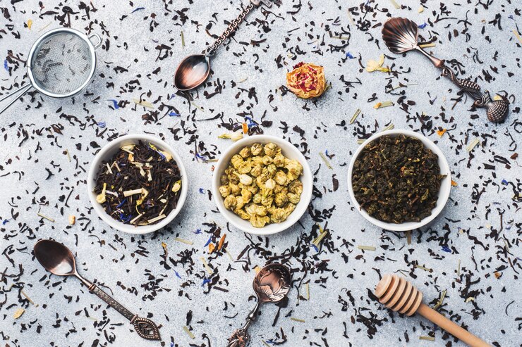 Variedad de hojas de té y de flores secas en cuenco en fondo gris.