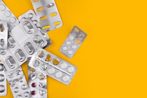 Una variedad de píldoras en ampollas en una pared amarilla copia espacio. Medicamentos