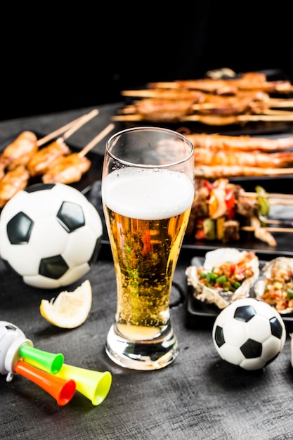 Una variedad de platos de barbacoa y cerveza se colocan en el fondo de madera negra Mirar fútbol y comer barbacoa