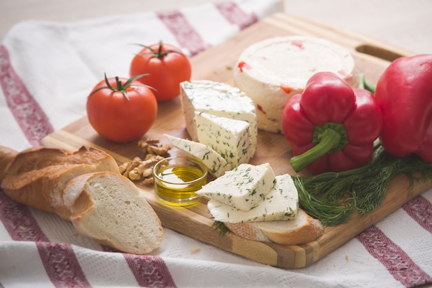 Variedad de queso casero y paprica y hierbas, aceite de oliva, aceitunas y pan sobre una tabla de madera