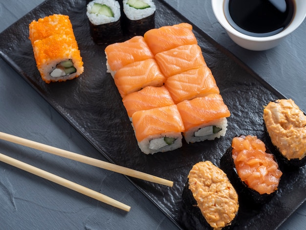 Una variedad de rollos japoneses y sushi en un plato con textura. Vista lateral. palitos de bambú de jengibre y salsa cerca.