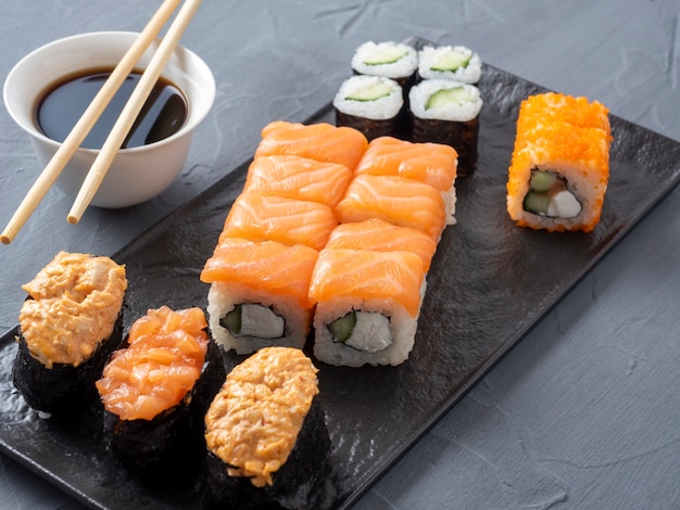 Una variedad de rollos japoneses y sushi en un plato con textura. Vista lateral. palitos de bambú de jengibre y salsa cerca.