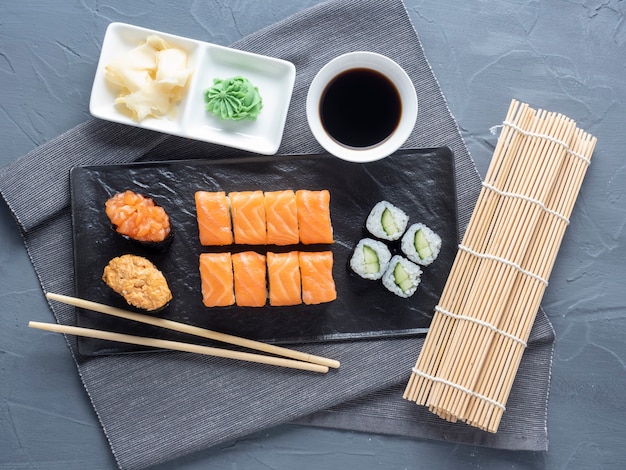 Una variedad de rollos y sushi gunkan anidados en un plato negro. al lado hay palitos de bambú y salsa de wasabi. Vista superior, endecha plana. cocina tradicional japonesa