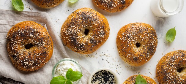 Variedade de bagels frescos de grãos inteiros com sementes de papoula, sementes de gergelim e ingredientes para o café da manhã em um fundo claro de concreto ou pedra. Foco seletivo. Vista do topo. Copie o espaço.