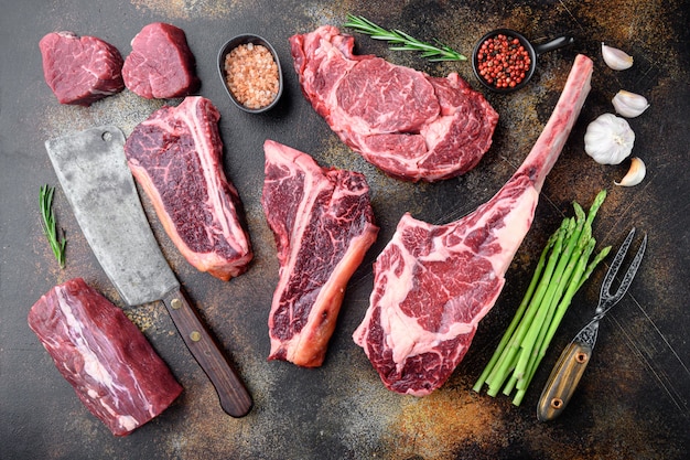 Foto variedade de bifes crus black angus prime, machadinha, t bone, club steak, costela de lombo e cortes de filé mignon, em uma velha mesa rústica escura, vista de cima plana lay