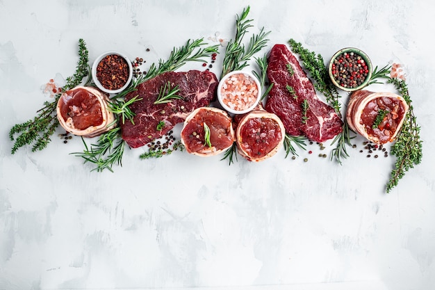 Variedade de bifes de carne crua para grelhar com temperos em um fundo claro. banner, vista superior da receita do menu.