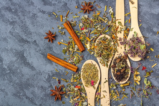 Variedade de chá differentdry em colheres de madeira com anis e canela em estilo rústico. Chá orgânico de ervas, verde e preto com pétalas de flores secas para a cerimônia do chá.