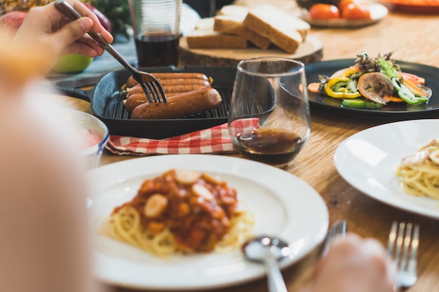 Variedade de comida na mesa de madeira e amigos jantando juntos.