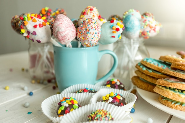 Variedade de doces decorados, bolinhos e biscoitos em uma mesa de madeira branca