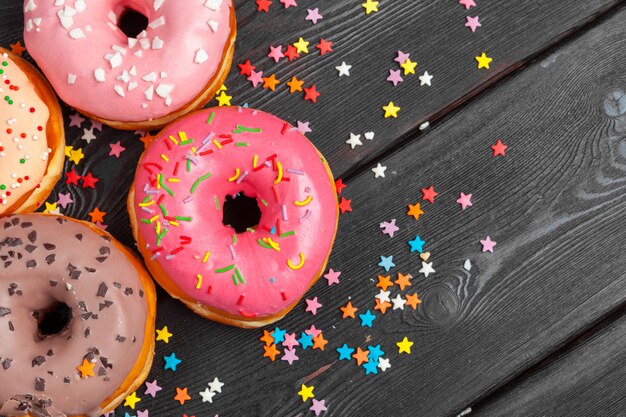 Variedade de donuts coloridos decorados com confetes coloridos granulado na superfície de madeira escura