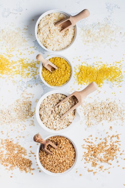 Variedade de flocos de cereais, arroz, milho, trigo sarraceno, aveia. superalimento em tigelas de cerâmica branca na mesa de madeira clara.