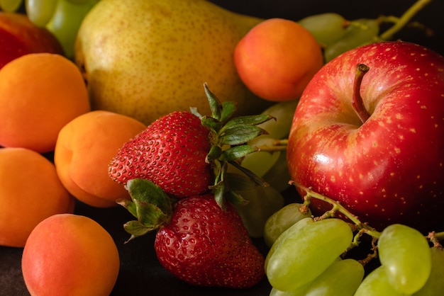 Variedade de frutas frescas uvas morangos damascos pêra maçã na superfície preta