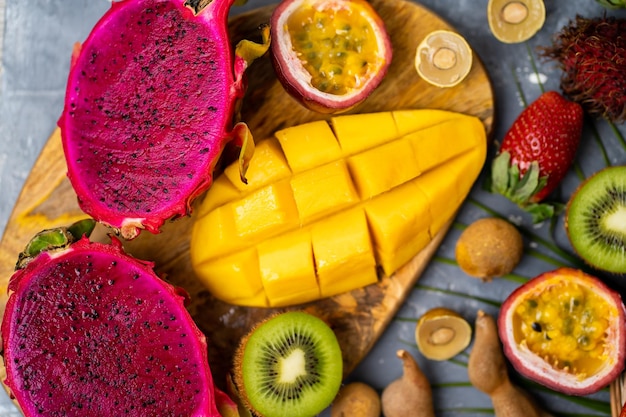 Foto variedade de frutas orgânicas exóticas tropicais. plano de fundo cinza. postura plana da composição de verão. vista de cima, closeup tiro de frutas suculentas frescas fatiadas na tábua de madeira.