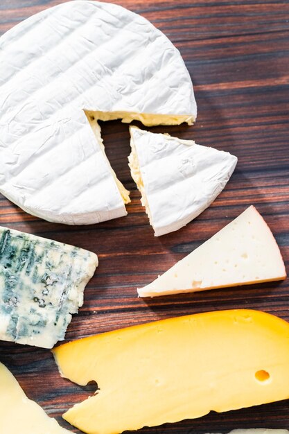 Variedade de grandes fatias de queijo gourmet em um fundo escuro de madeira.