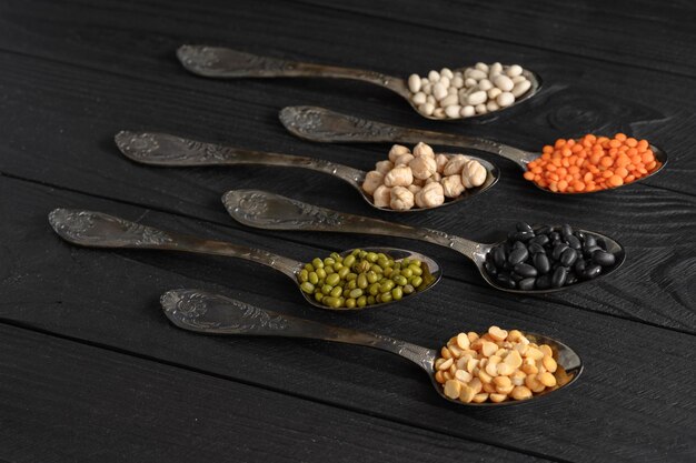 Variedade de legumes em colheres de prata velhas em um fundo preto de madeira