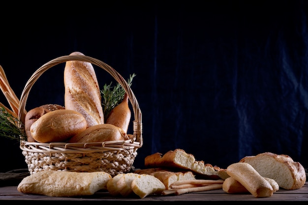 Variedade de pães na cesta na mesa de madeira no escuro