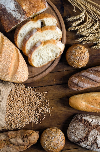 Variedade de pão, espigas e grãos de trigo na mesa de madeira. Estilo rústico, vista de cima.