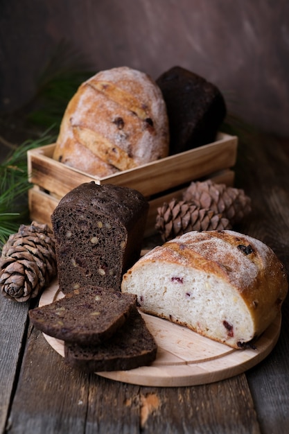 Variedade de pão fermentado caseiro marrom e branco com nozes de cedro em fundo de madeira escura