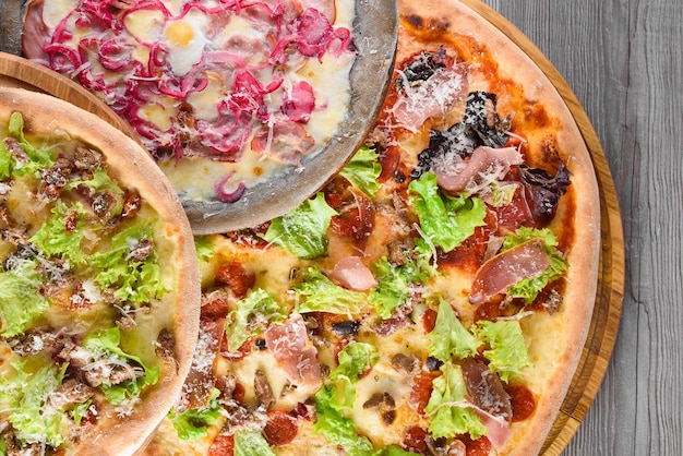 Variedade de pizzas com carne, salame, presunto, tomate, mussarela, parmesão, salada, cebola azul, ovo de codorna em placas de madeira. Vista do topo.